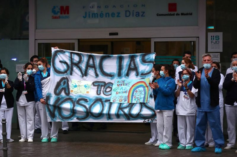 Работники больницы Fundacion Jimenez Diaz держат плакат с надписью «Спасибо всем», в то время как люди аплодируют им со своих балконов, Мадрид, Испания. 