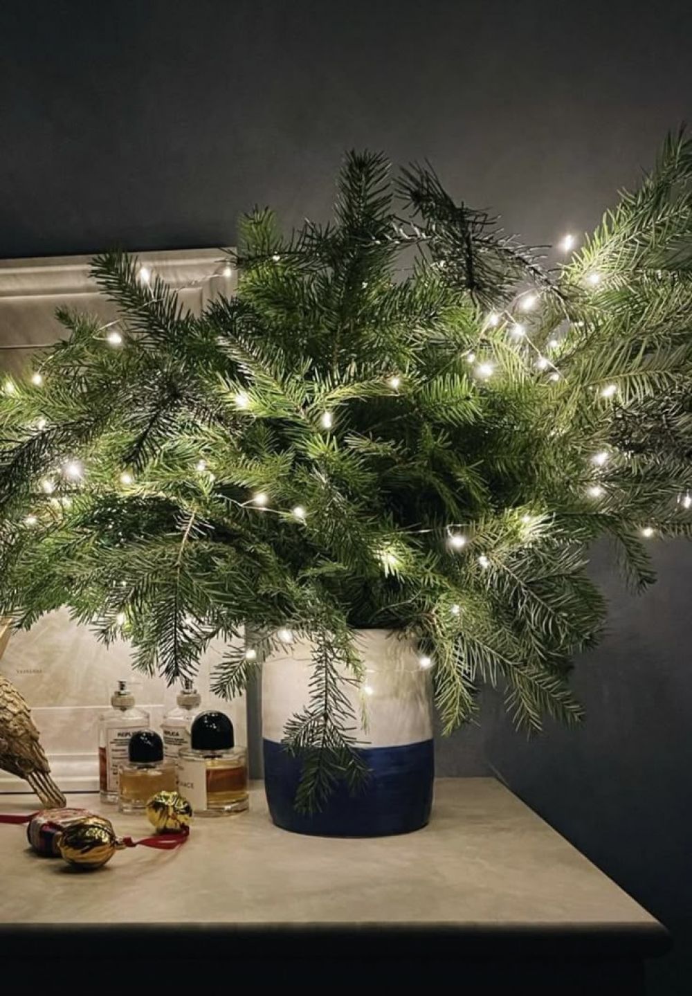 Используйте ветки нобилиса или искусственные лапки ёлки, чтобы создать очаровательные композиции для прикроватной тумбочки или праздничного стола. Оживите зелень с помощью тонкой нити мерцающих огоньков и/или добавьте миниатюрные игрушки.